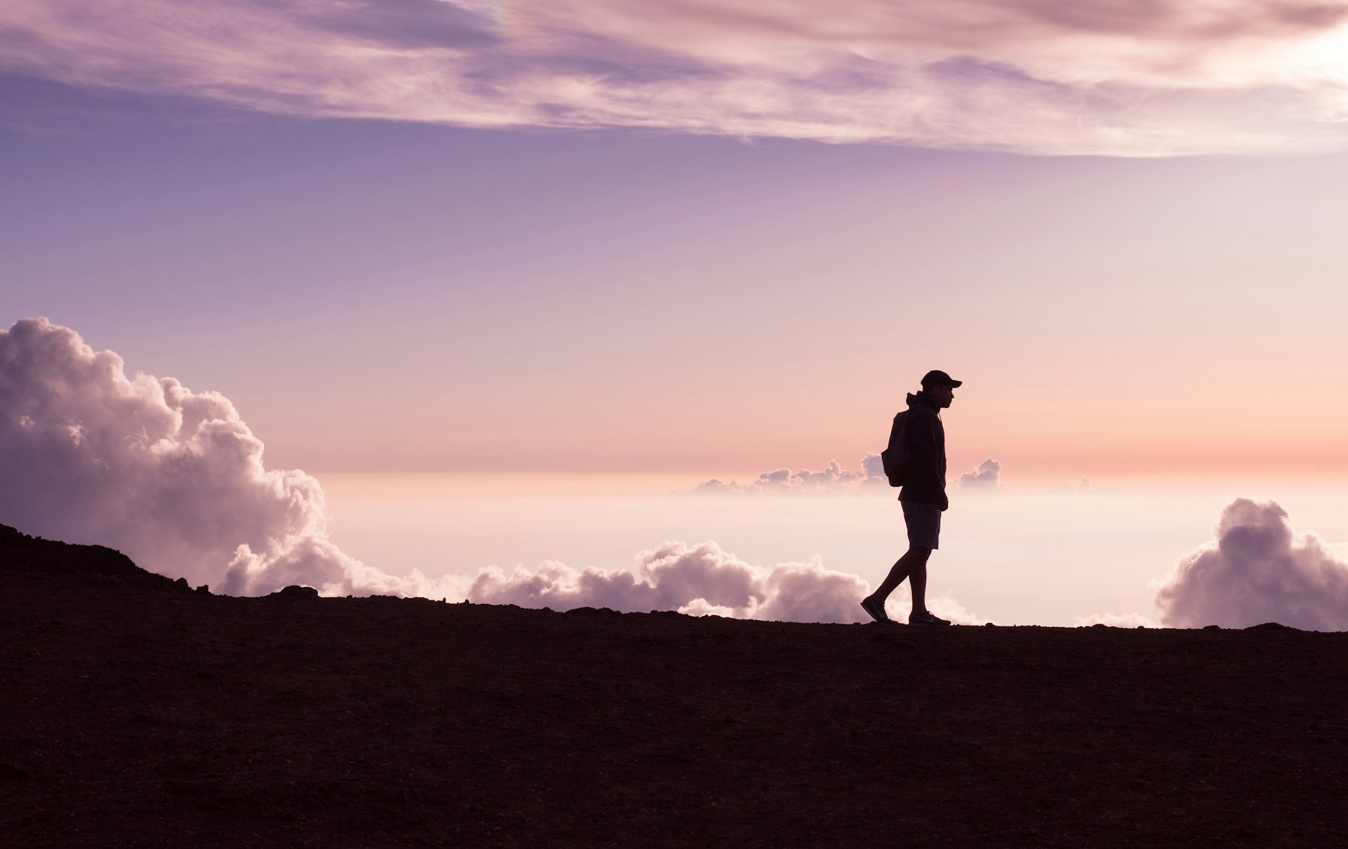 A walker silhouetted against a pink and violet sunset sky above the clouds
